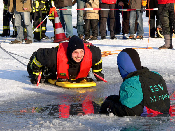 Auf einem Schlitten arbeitet sich ein Feuerwehrmann mit Haken zum Eingebrochenen vor. Auf einem Schlitten arbeitet sich ein Feuerwehrmann mit Haken zum Eingebrochenen vor.